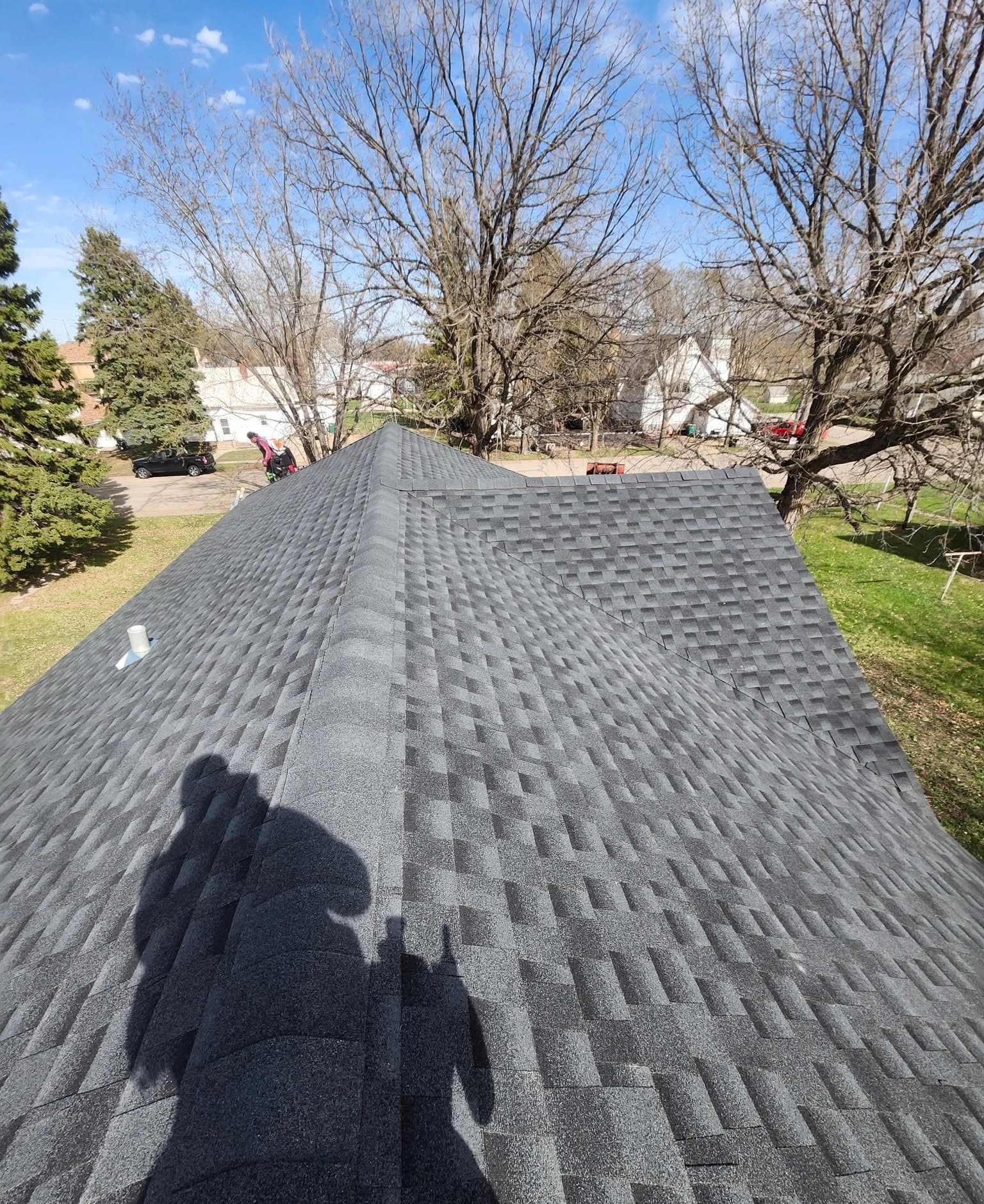Curtis's shadow across a freshly finished charcoal shingle roof on a spring day