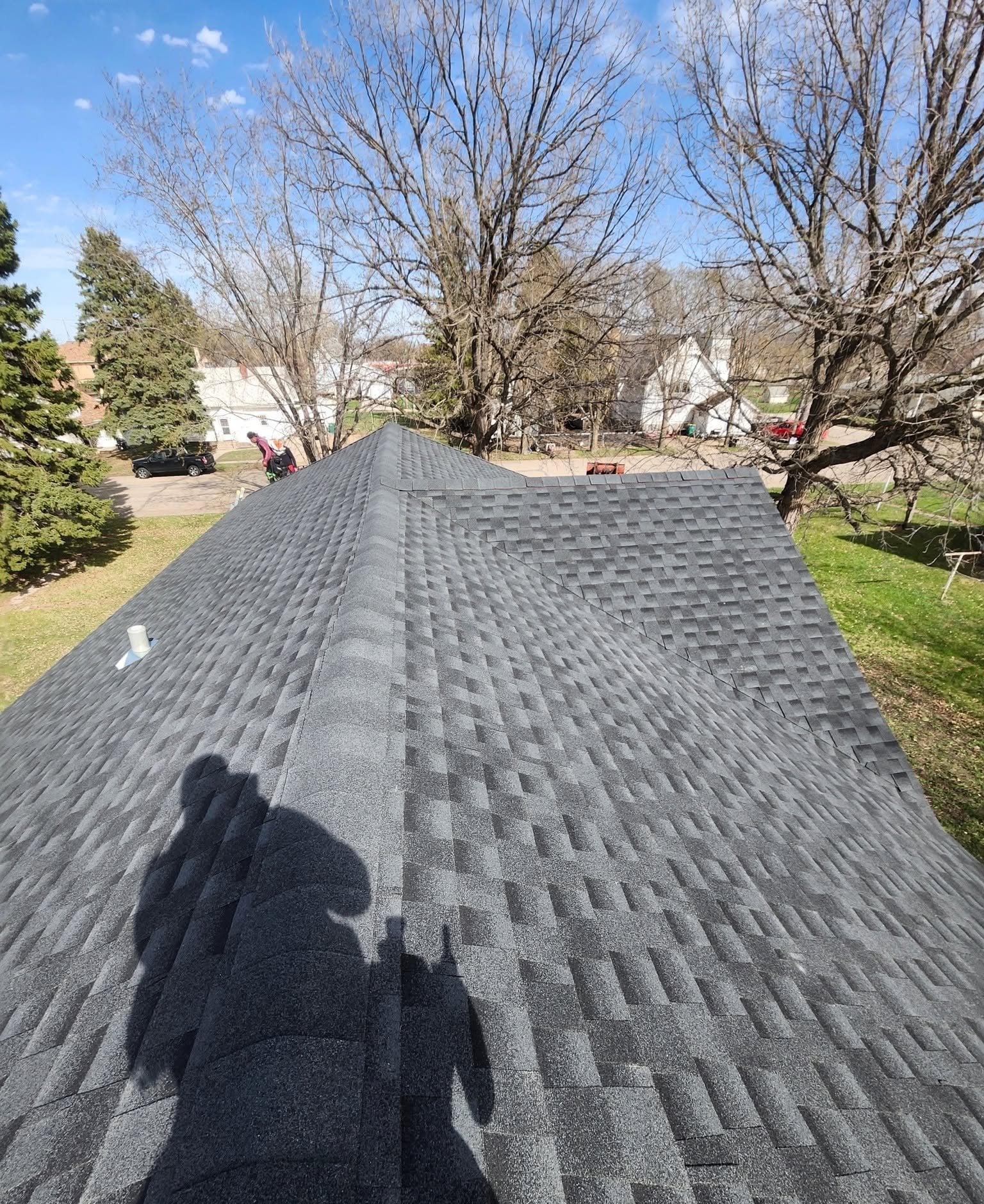 Curtis's shadow falls across a freshly finished charcoal shingle roof on a spring day