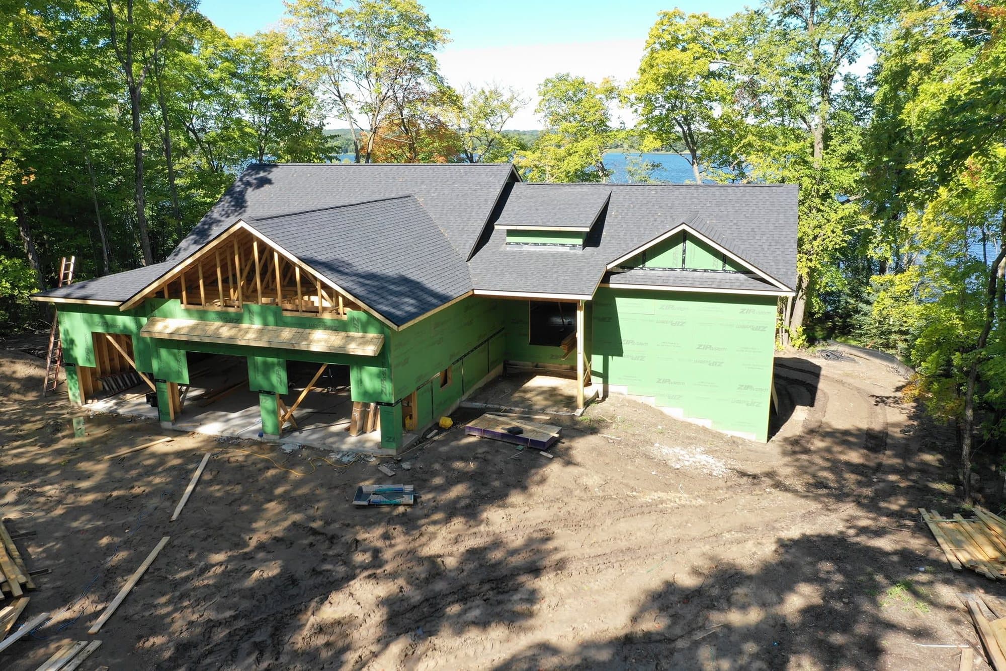 New lake home with a gray shingle roof, water visible through the trees