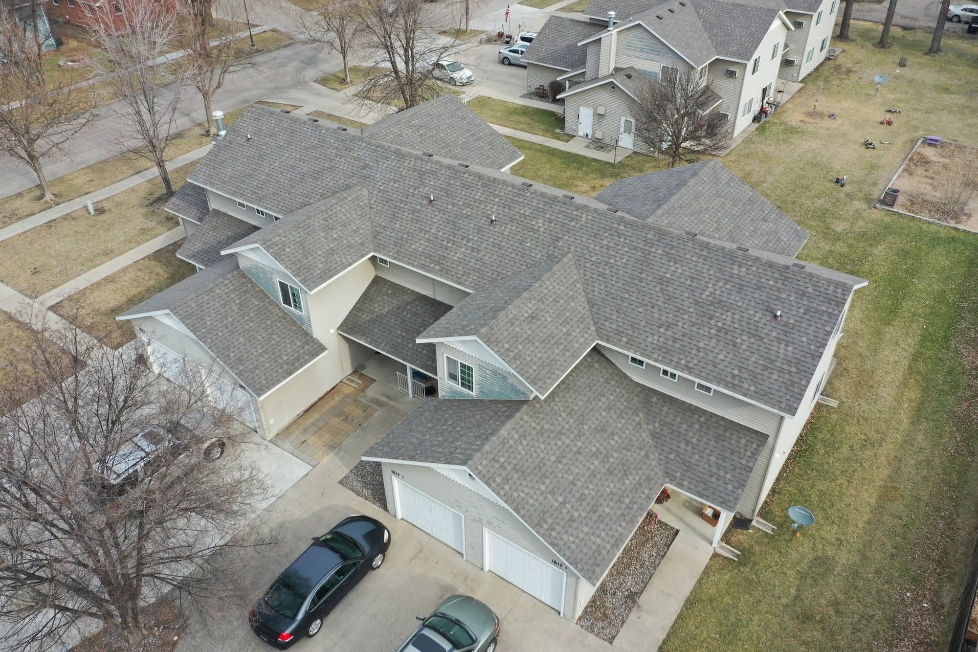 Twin home with a new gray shingle roof, seen by drone in early spring